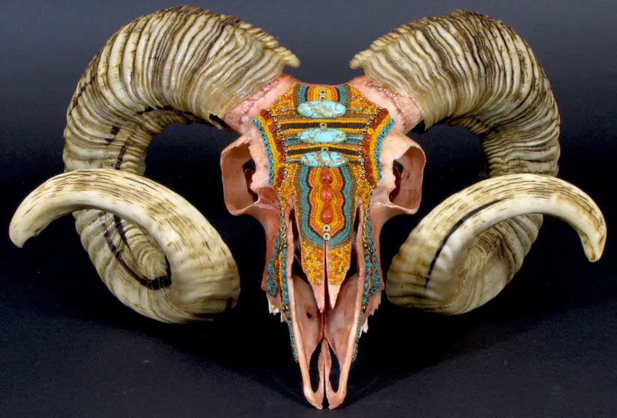 A ram skull with horns and turquoise painted on it.