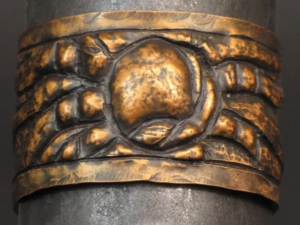 A Copper Chase Repousse Cuff with a design on it.