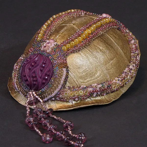A beaded turtle hat with purple beads.