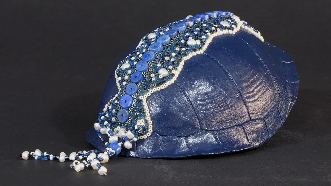 A blue turtle hat with pearls and beads.