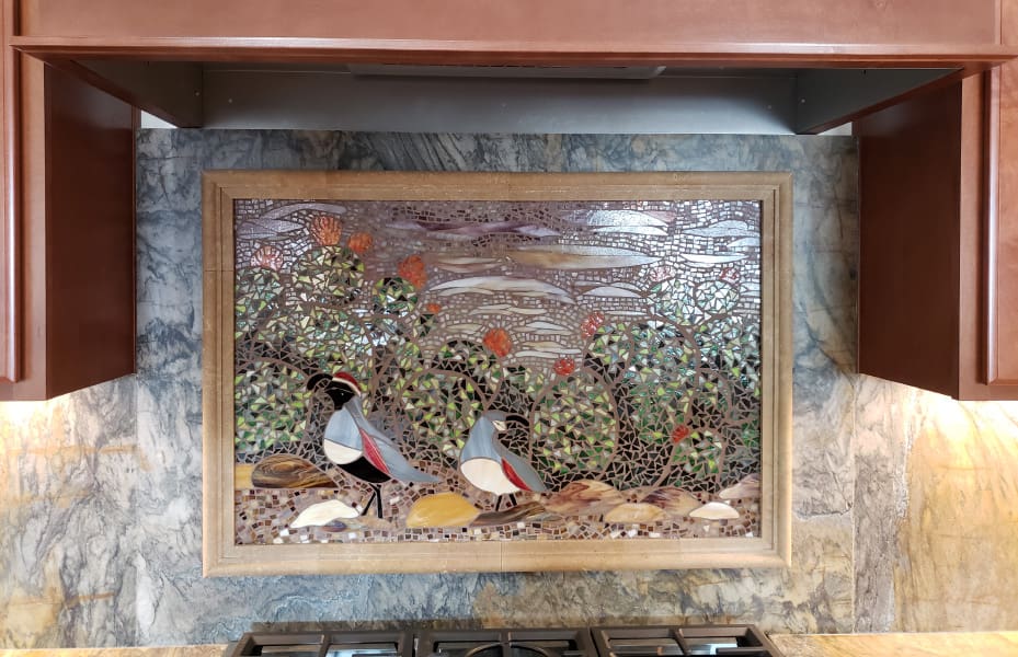 A kitchen with a tiled backsplash with birds and cactus.