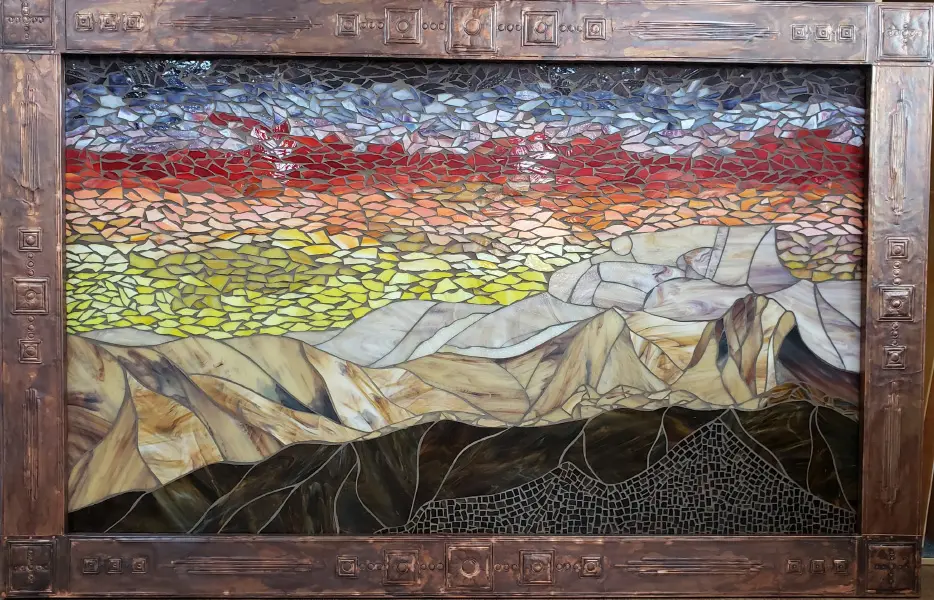 A stained glass window with mountains in the background.