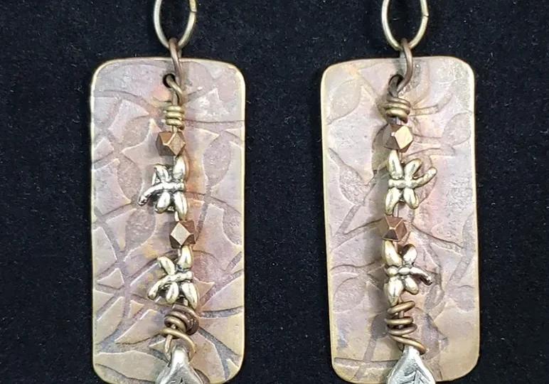 A pair of Copper Stamped With Bead Accent Earrings with leaves and flowers on them.