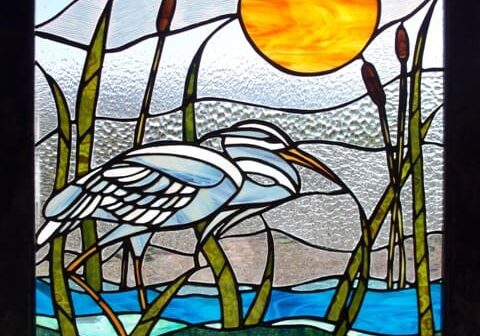 A stained glass window with a white heron and reeds.