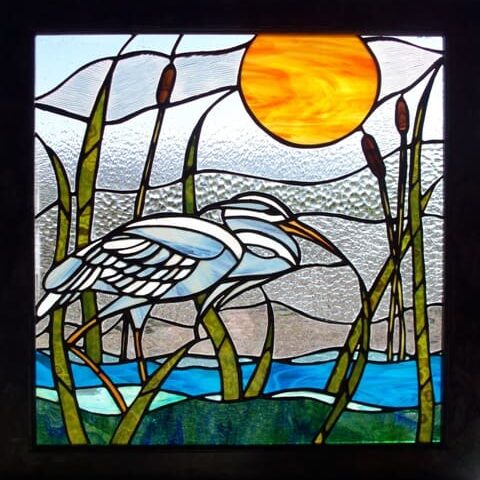 A stained glass window with a white heron and reeds.