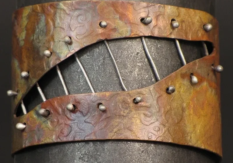 A Copper, Flame Painted Cuff With Sterling Silver Accents with rivets on it.